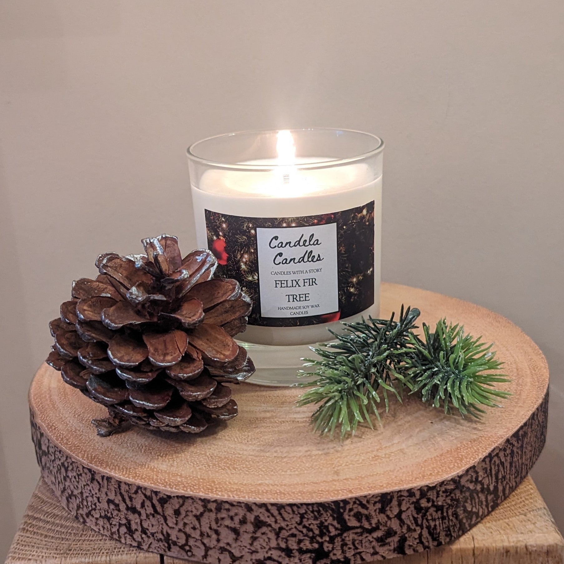 Candle with a pine cone and greenery on a wooden surface