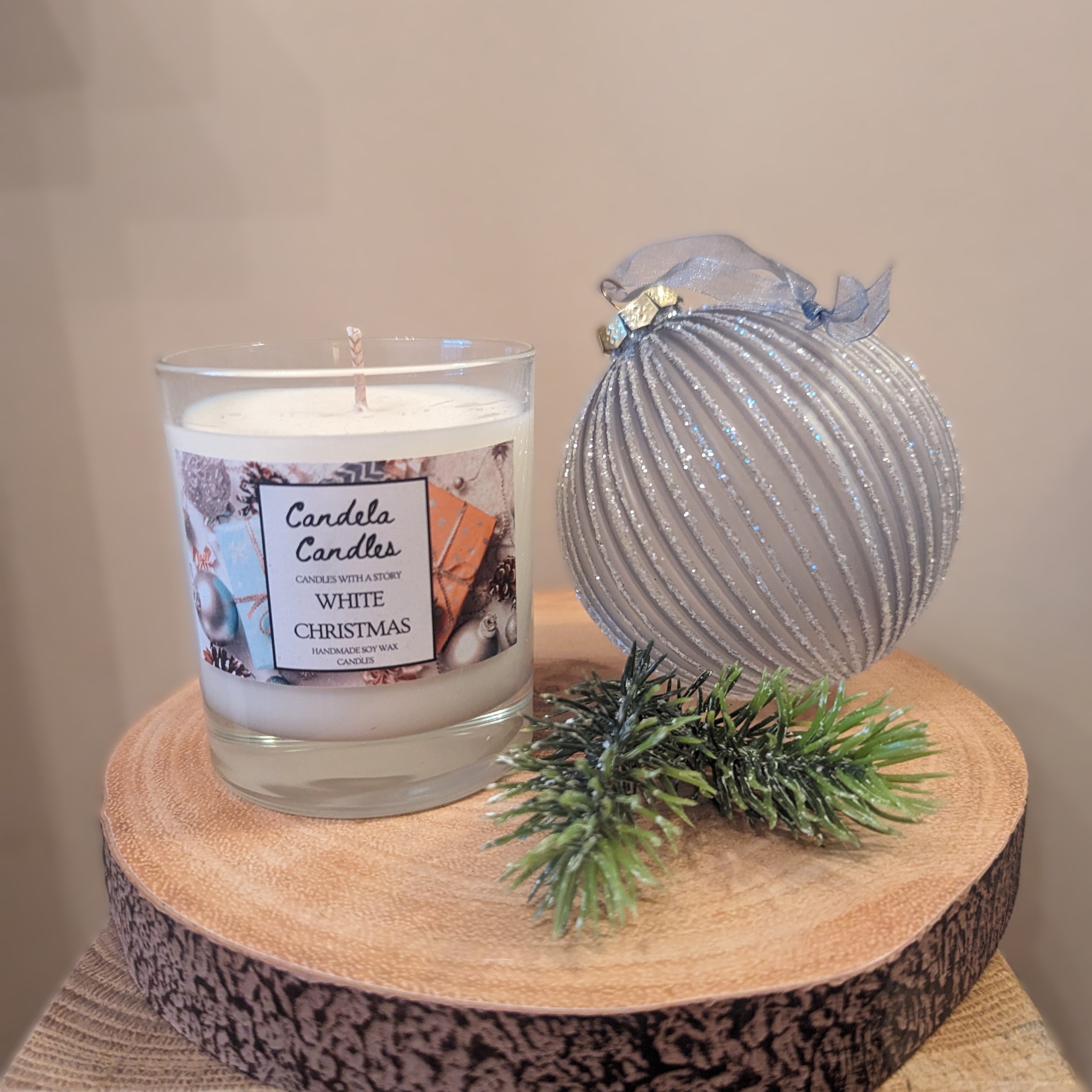 Candle labeled 'White Christmas' with a decorative ornament and greenery on a wooden surface.